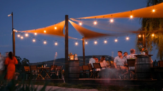 Custom triangular shade sails stretched over an outdoor dining area, providing stylish sun protection and a welcoming atmosphere with warm string lighting.