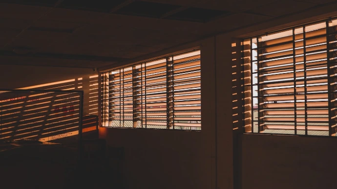 Warmw ood-tone horixontal blinds on multiple windows, filtering golden sunlight and casting elegant shadows while complementing natural interior finishes.