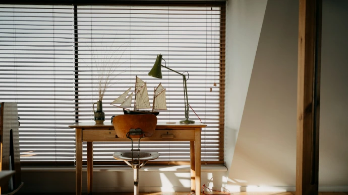 Wooden desk with model ship and lamp by window