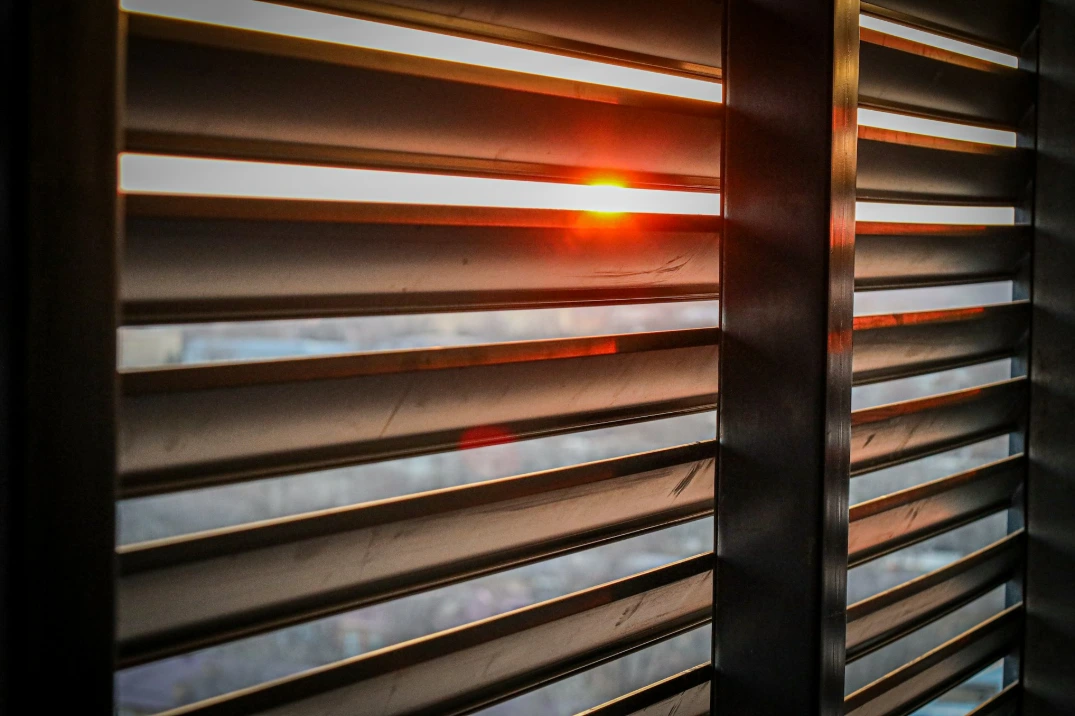 Close-up of plantation shutters with adjustable horizontal louvers, allowing warm sunlight to filter through while adding architectural style and privacy.