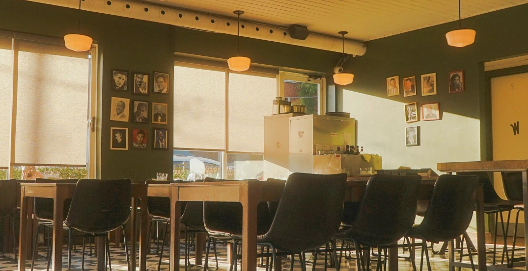 Custom light-filtering roller shades on large cafe windows, softly diffusing sunlight, reducing glare, and complimenting a modern commercial interior.
